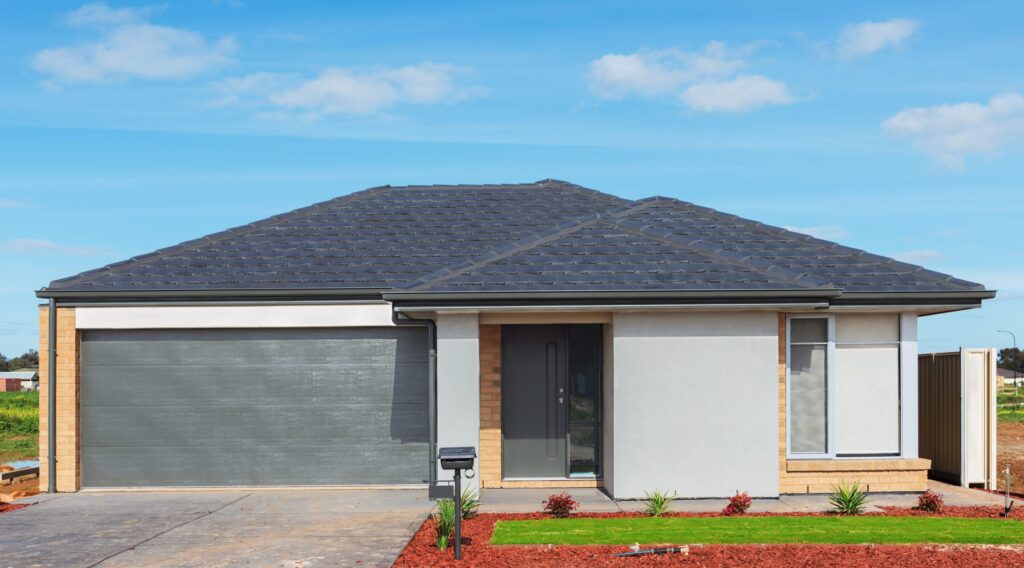 new brick house with green lawn and plants and garage to illustrate Why do garage doors need springs